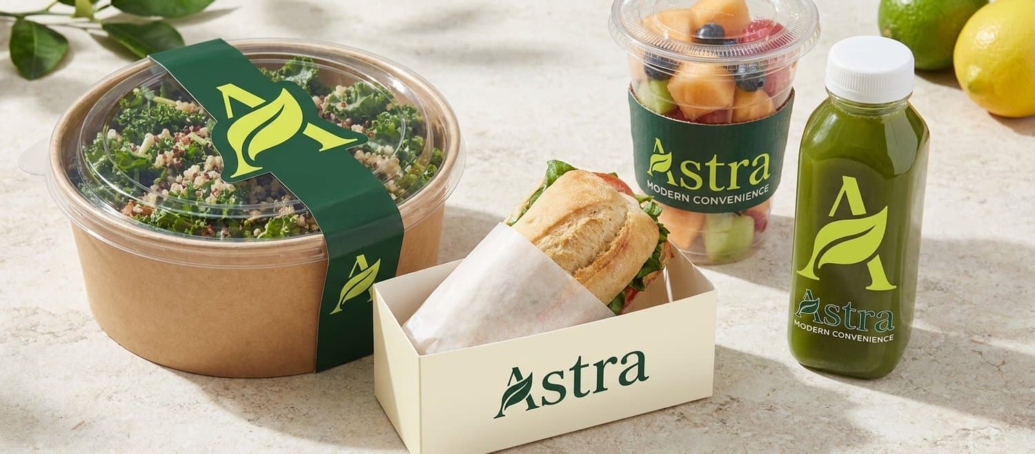 Astra grab-and-go — a kale grain salad, a baguette sandwich, a fruit cup, and a cold-press green juice.